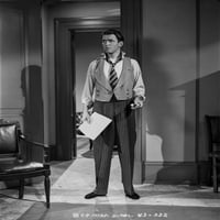 Джеймс Стюарт, стоящ в костюм на сива жилетка и бяла риза с дълъг ръкав с дясна ръка, която държи хартиена снимка отпечатък